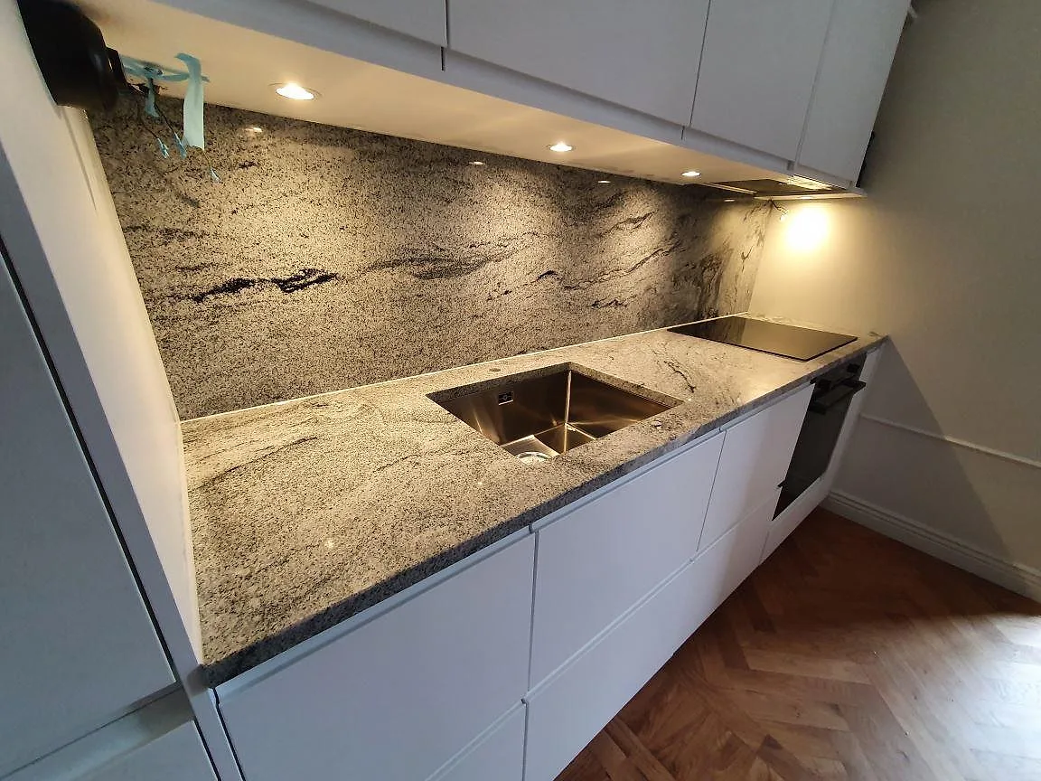 Vinklad vy av köksbänkskiva i Viscont White granit i Stockholm med synlig grågrafisk ådring, underlimmad diskho och induktionshäll, polerad yta.