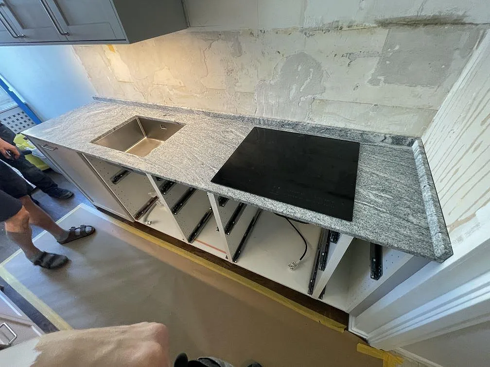 Lång köksbänkskiva i polerad Viscont White granit med diskho och svart häll under montering i Stockholm.