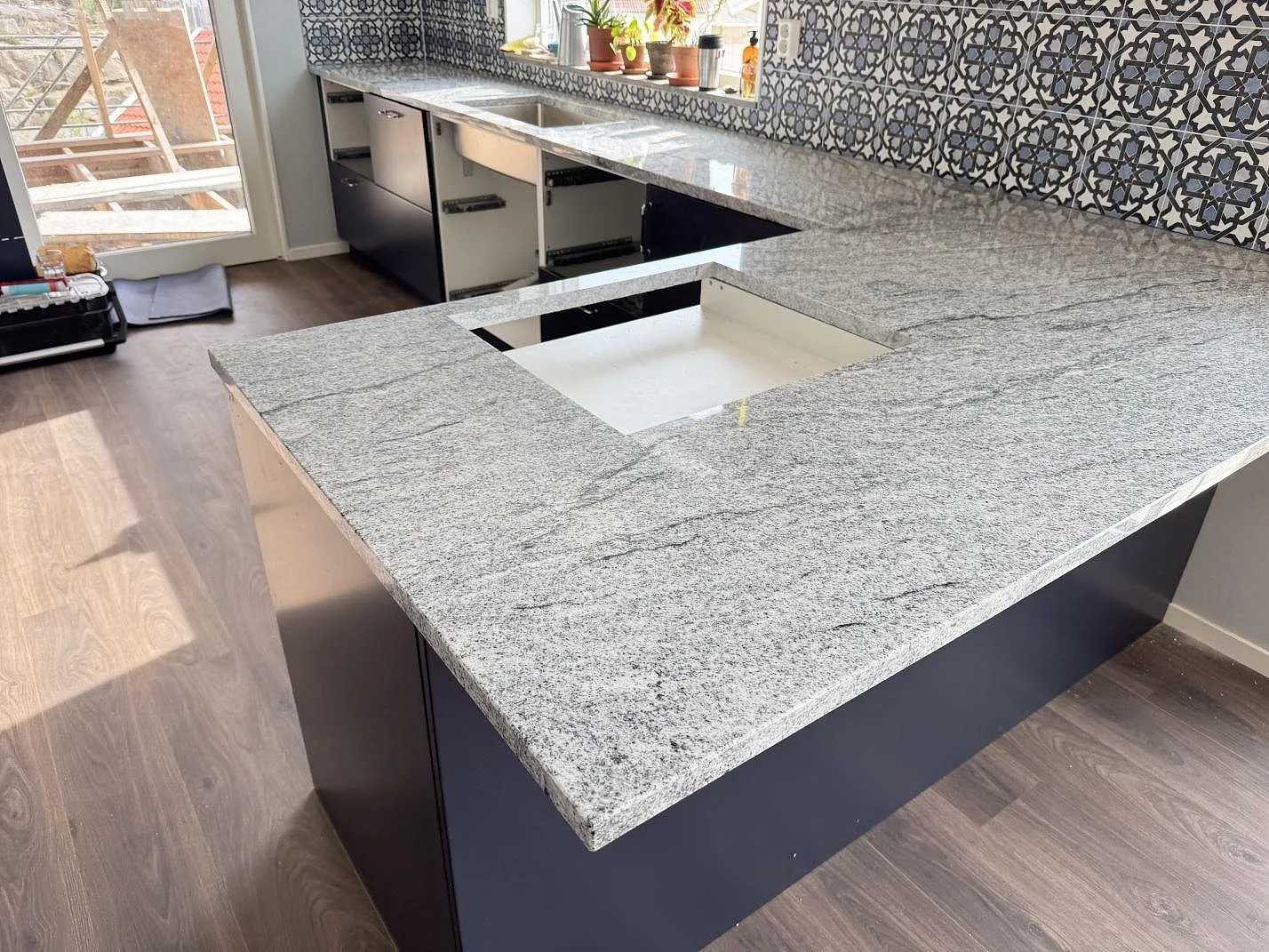 Köksbänkskiva och köksö i polerad Viscont White granit i ett kök i Väjern, med rektangulärt urtag och öppen montering.
