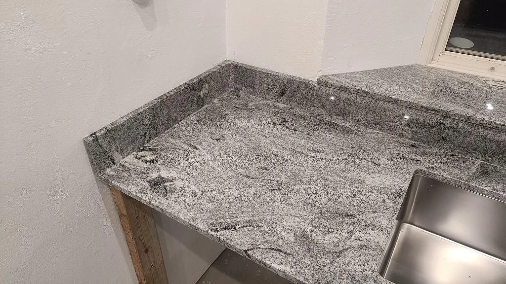 Detalj av polerad Viscont White granit vid underlimmad rostfri diskho och uppvikt stänkkant i ett kök i Vellinge.