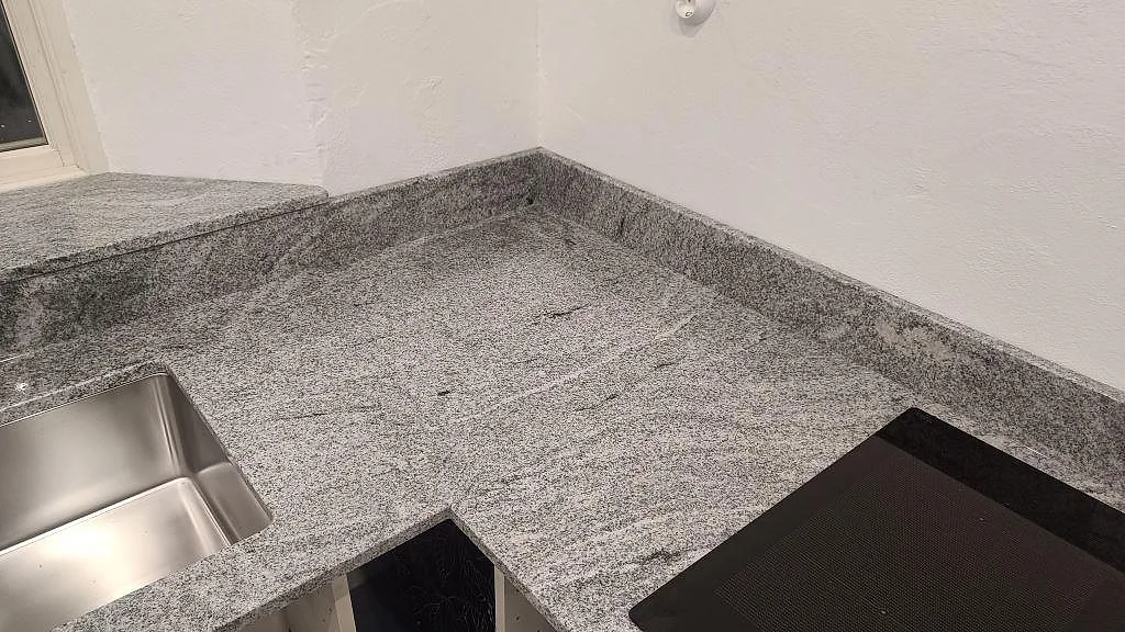 Hörndel av köksbänkskiva i polerad Viscont White granit med diskho, häll och stänkkant i Vellinge.