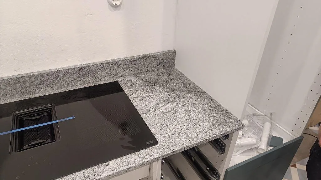 Sidodel av köksbänkskiva i polerad Viscont White granit bredvid induktionshäll och vita köksstommar i Vellinge.