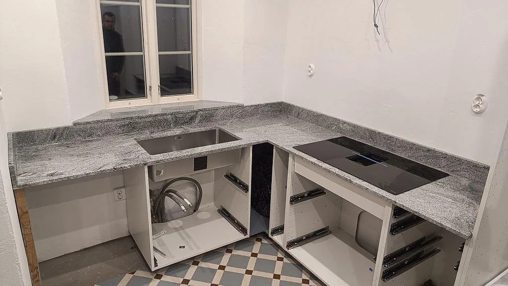 U-formad köksbänkskiva i polerad Viscont White granit med underlimmad rostfri diskho och induktionshäll i ett kök i Vellinge.