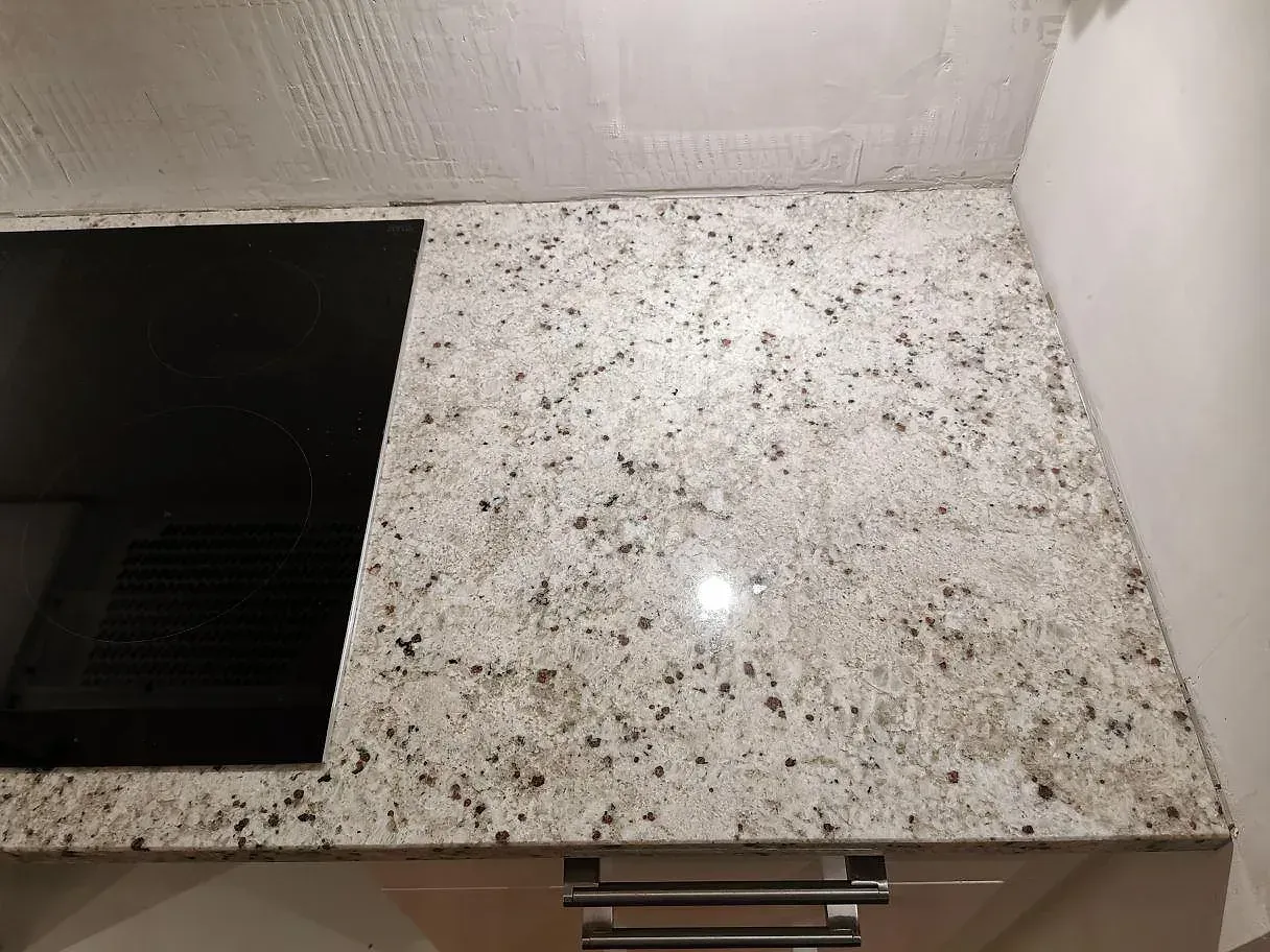Hörn av polerad Colonial White granitbänkskiva med den grå- och rödbrunspräckliga ådringen i ett kök i Lomma.
