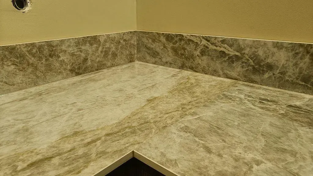 Hörndetalj av köksbänkskiva i Dekton Taga med uppvikt stänkkant som visar den ljusgrå keramikens ådring i Göteborg.