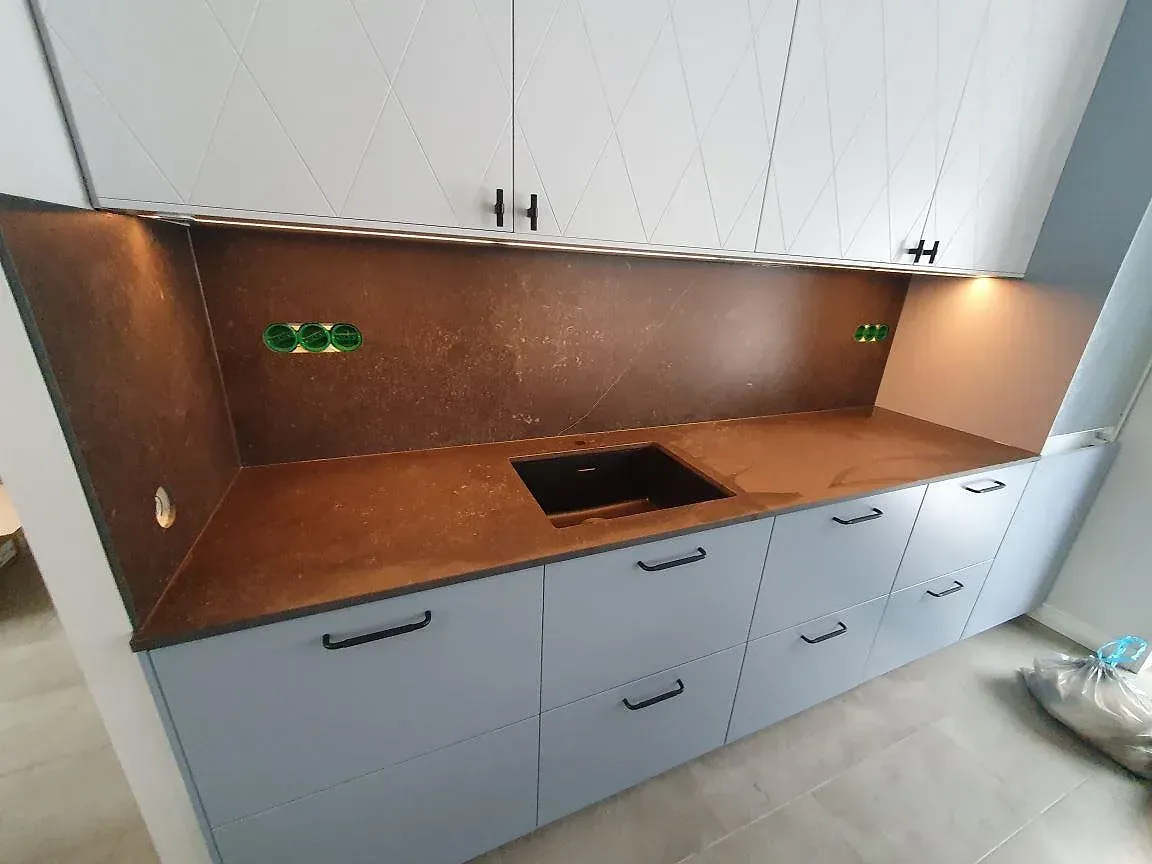 Köksbänkskiva i varm brun Dekton Fossil, matt yta, med underlimmad svart kompositdiskho och uppvikt väggbeklädnad i samma sten i ett kök i Ekerö.