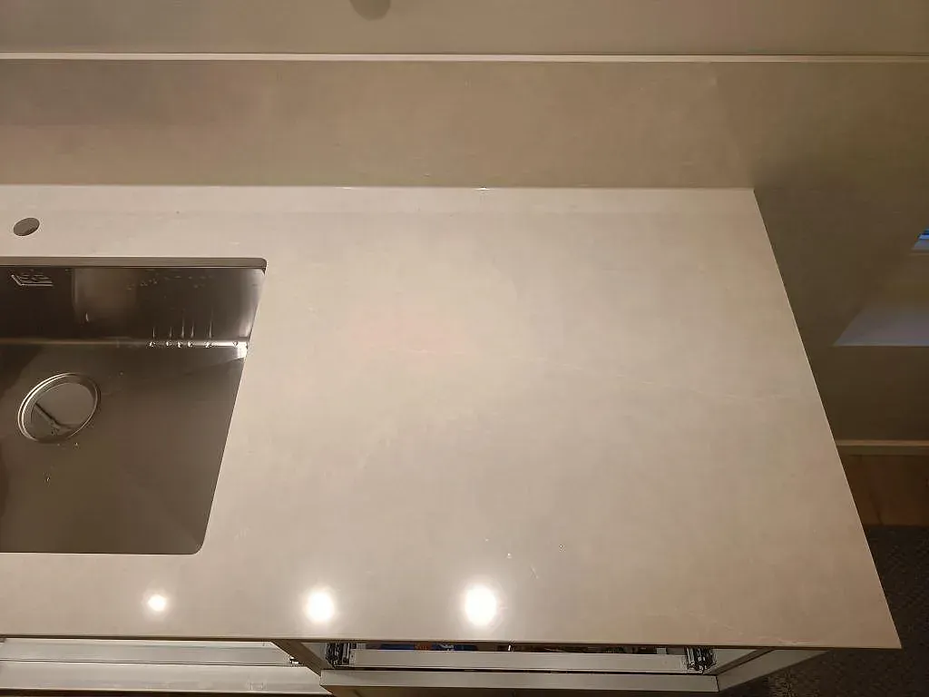 Detalj av matt Jura Grey bänkskiva med uppvikt stänkskydd och fossilådring vid fönstret i ett kök i Limhamn.