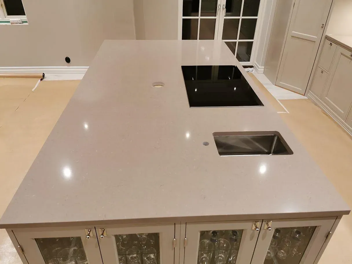 Köksö i Silestone Coral Clay med övermonterad induktionshäll och liten underlimmad spolho i rostfritt, polerad yta, kök i Kristianstad.