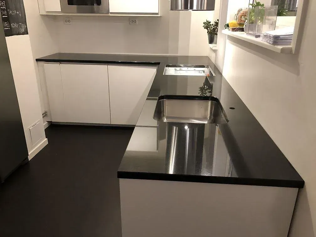 Köksbänkskiva i svart Nero Assoluto granit, polerad, i ett U-format vitt kök i Skövde med underlimmad rostfri diskho och håltagning för häll.