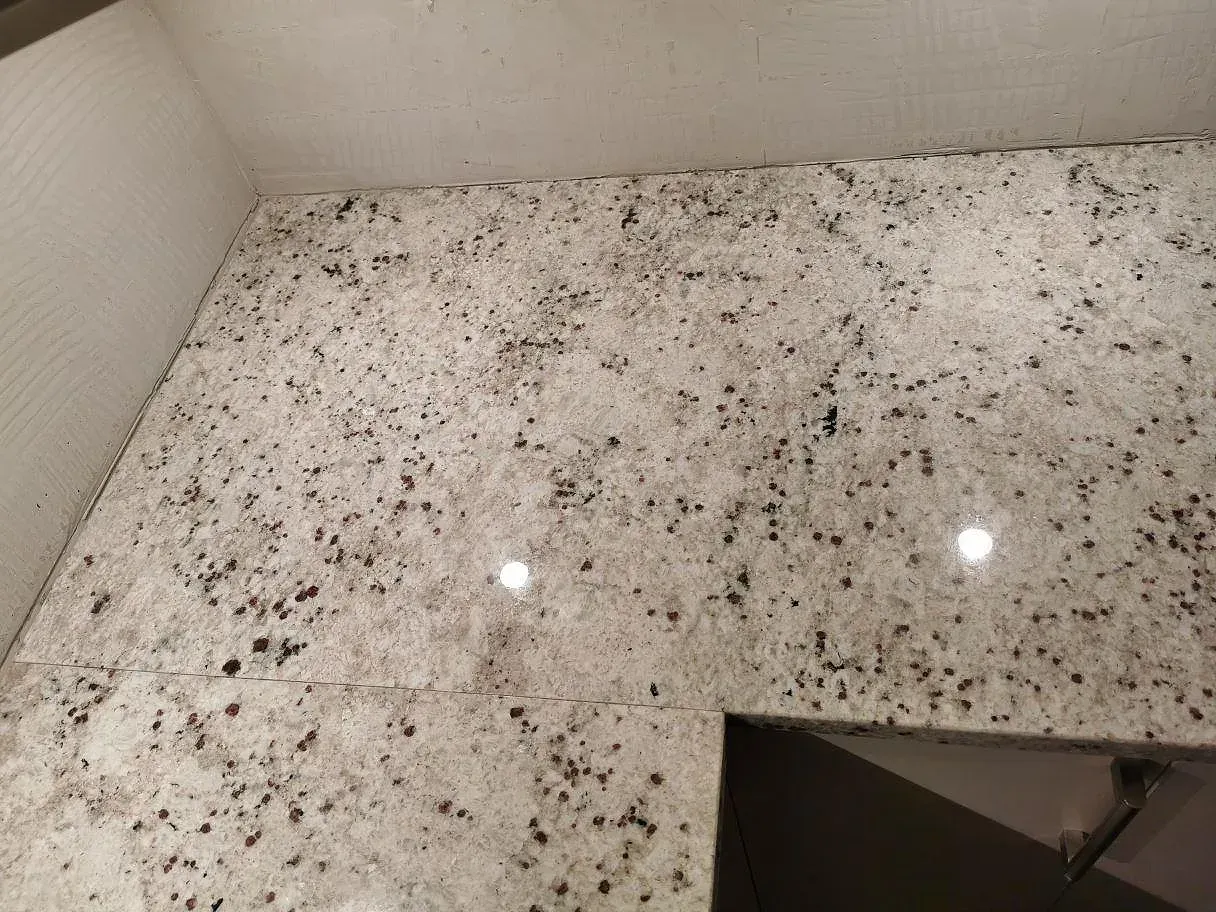 Svart induktionshäll monterad ovanpå en polerad Colonial White granitbänkskiva i ett kök i Lomma.