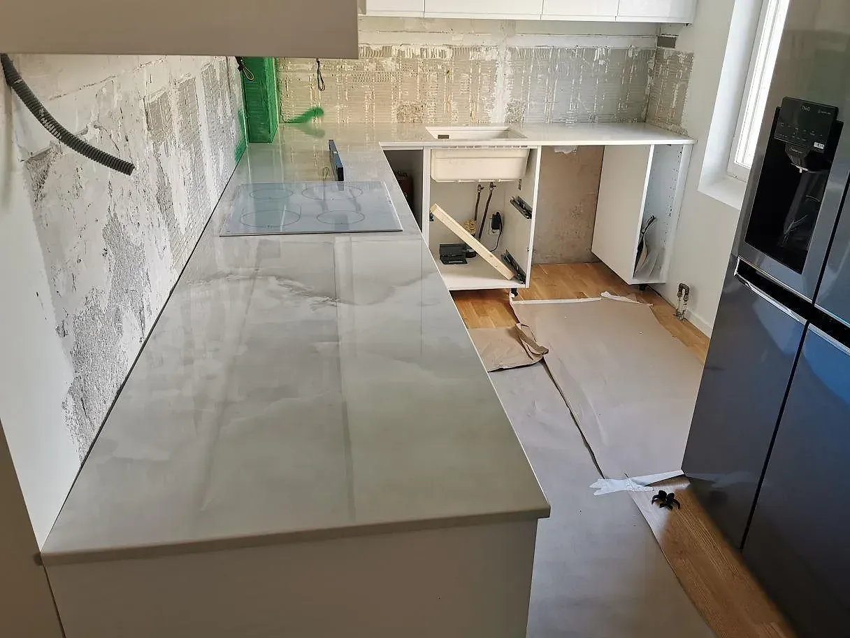 Köksbänkskiva i ljus Dekton Helena med marmorlik ådring, induktionshäll och nedsänkt diskho längs väggen i ett kök i Malmö.