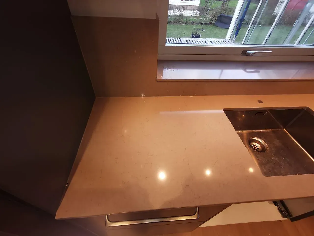 Köksbänkskiva i Silestone Coral Clay, polerad varm greige kvartskomposit, med underlimmad rostfri diskho vid fönstret i ett kök i Malmö.