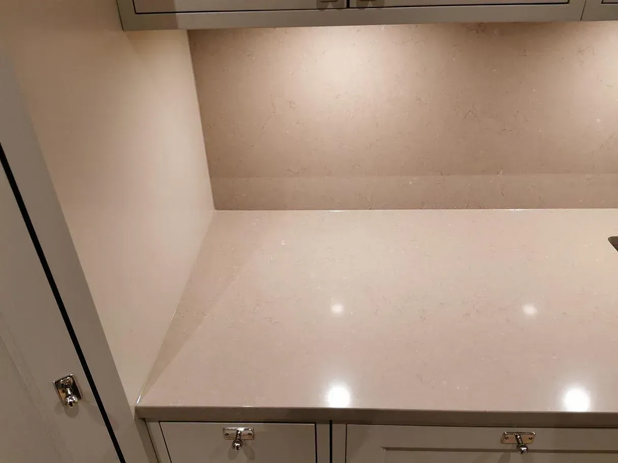 Polerad bänkskiva i Silestone Coral Clay mot uppvikt stänkkant i samma sten längs köksväggen i Kristianstad.