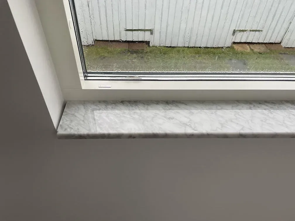 Polerad fönsterbänk i vit marmor Carrara C monterad under ett fönster med ådring tydligt synlig, i ett hem i Lund.