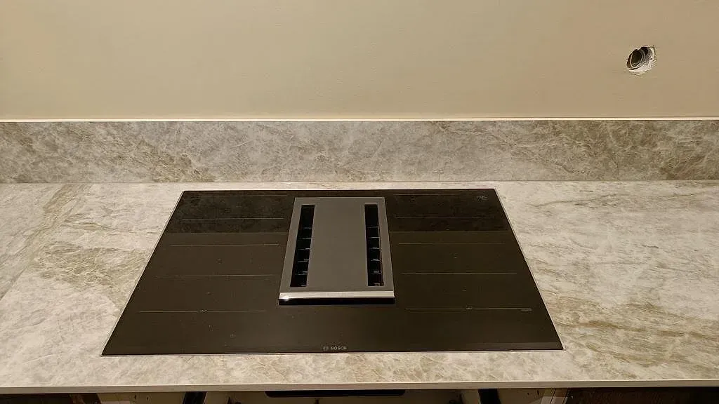 Övermonterad svart Bosch induktionshäll med integrerad fläkt i en bänkskiva av Dekton Taga keramik i ett kök i Göteborg.