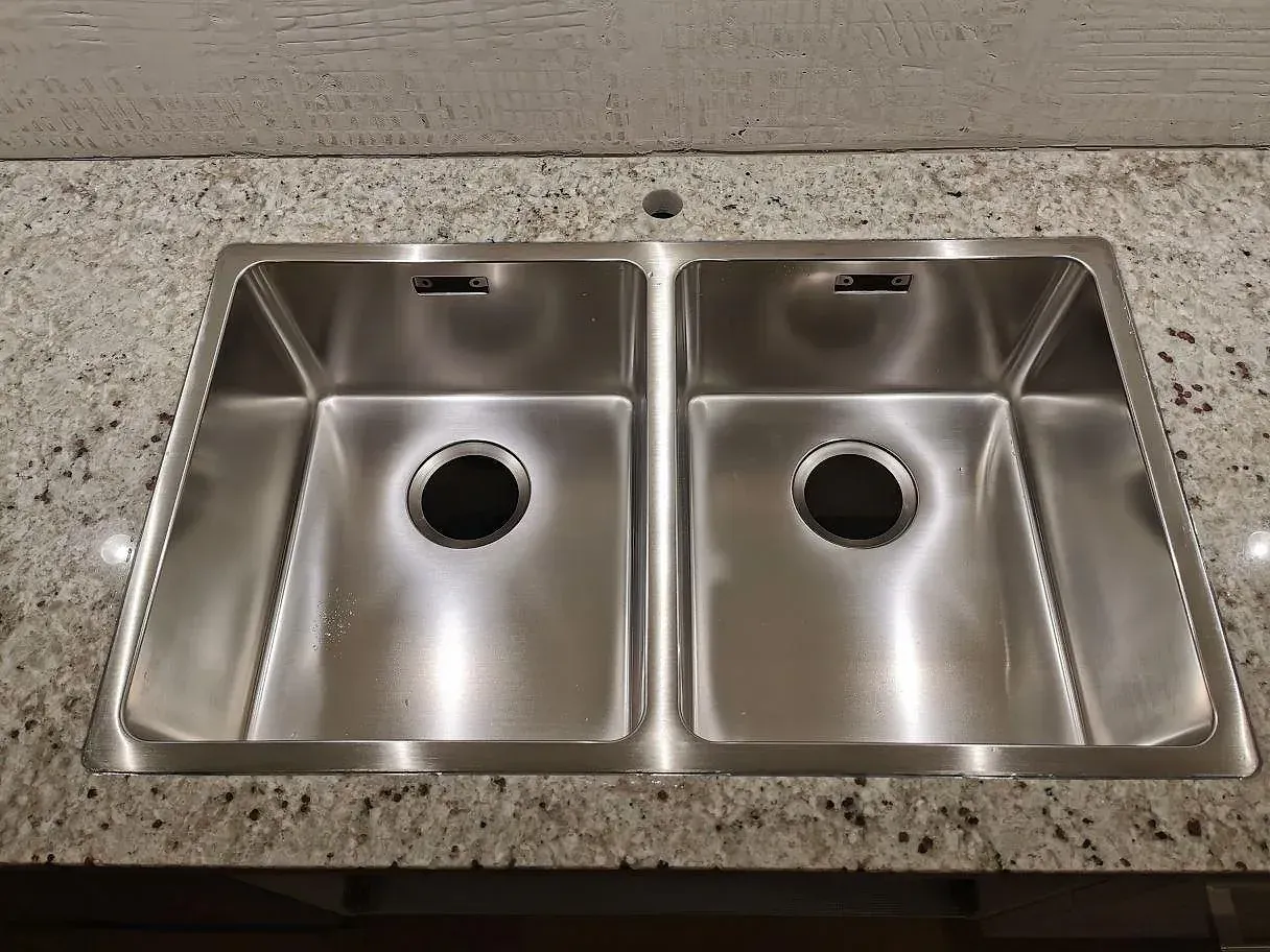 Rostfri diskho monterad i nivå med polerad Colonial White granit, närbild på den gräddvita spräckliga stenytan i ett kök i Lomma.